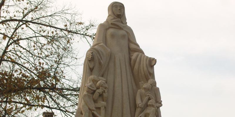  Die Statue ist eine Frau, neben der mehrere Kinder unter ihrem Mantel stehen und zu ihr hinaufschauen 