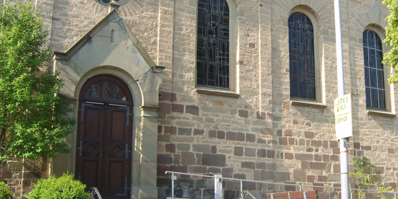  Links ist der Eingang zur Kirche, rechts sind drei Bleiglasfenster 