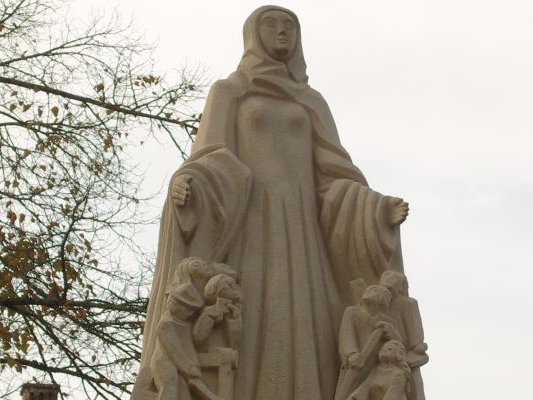 Die Statue ist eine Frau, neben der mehrere Kinder unter ihrem Mantel stehen und zu ihr hinaufschauen
