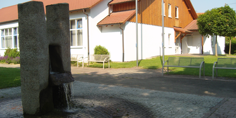  Links steht ein Steinbrunnen, dahinter sind mehrere Bänke 